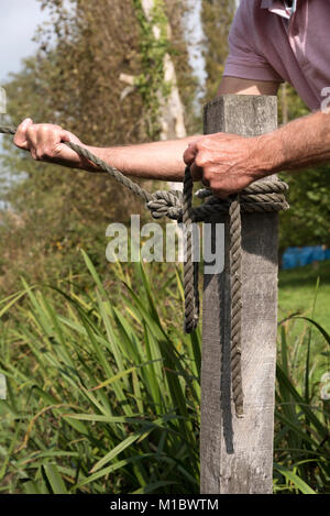 Mooring line being held in man's hands being attached to a post with a round turn and two half hitches knot Stock Photo