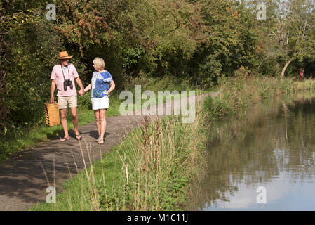 Couple carrying a picnic basket walking along a towpath next to the river Stock Photo