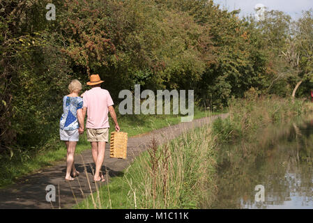 Couple carrying a picnic basket walking along a towpath next to the river Stock Photo