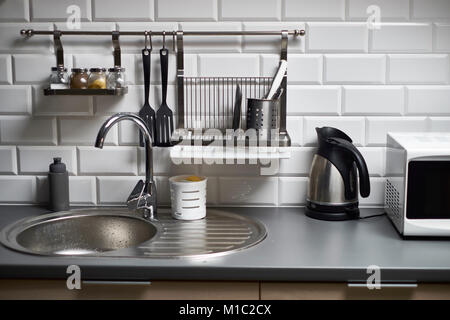 Kitchen in a loft style with concrete and brick walls and tiles, a sink, microwave, teapot and modern lamp. Stock Photo