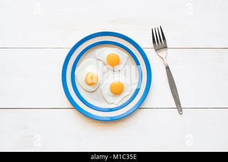 Fried Quail Eggs on a cornishware plate with a fork from above Stock Photo