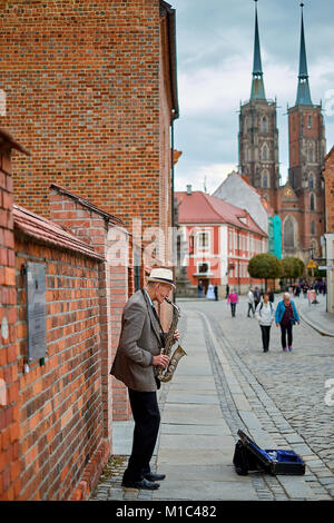 Street musician with saxophone on pedestrian Tumski Bridge with Cathedral of St. John the Baptist on the background. Wroclaw, Poland Stock Photo