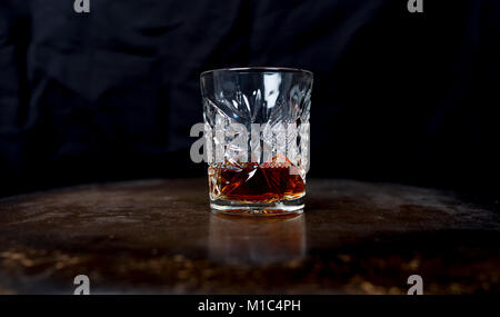 Whiskey (or whisky) in a luxury heavy cut crystal glass tumbler on a wooden table against a dark background Stock Photo