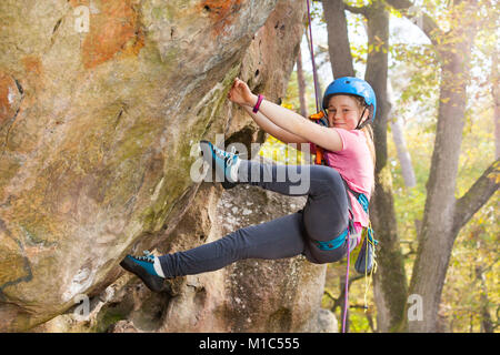 Teenage girl in helmet climbing on the rock route in forest area Stock Photo