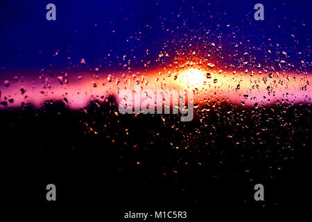 Rain drops texture on window glass with stunning colorful violet pink sunset light abstract blurred cityscape skyline bokeh background. Soft focus Stock Photo