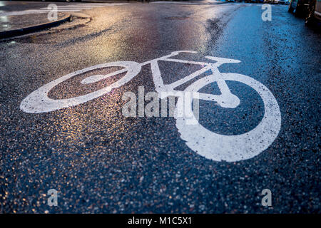 Beautiful lights reflections over the wet asphalt revealing a closeup bike sign during evening on a city street Stock Photo