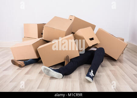 Close-up Of Couple Lying Under The Heap Of Cardboard Boxes On Floor Stock Photo