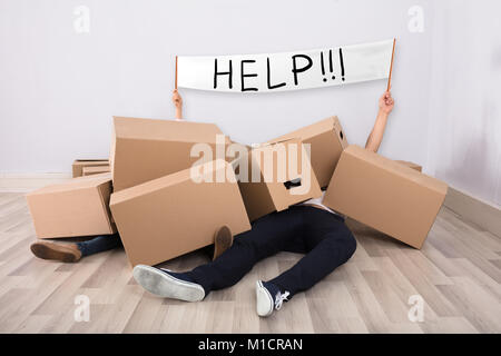Couple Lying Under The Heap Of Cardboard Boxes On Floor Showing White Help Flag Stock Photo