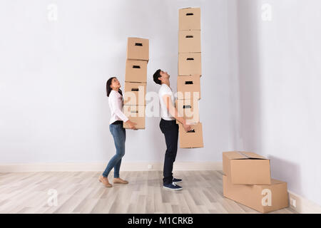 Young Couple Carrying Stack Of Cardboard Boxes In Their New Home Stock Photo