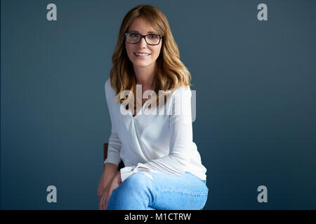 Beutiful mature woman wearing white shirt while looking at camera and smiling at dark background. Stock Photo
