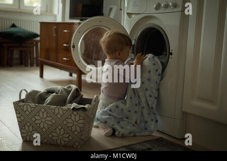 Baby putting clothes inside the washing machine Stock Photo