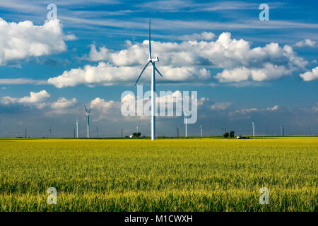 A wind mill farm cast against a deep blue sky contrasting with the white fluffy clouds. Stock Photo