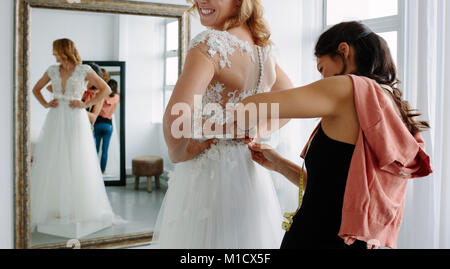 Female trying on wedding dress in a shop with women assistant. Female assisting bride getting dressed in wedding gown.