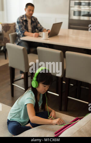 Girl using digital tablet while father using laptop in background Stock Photo