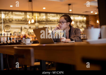 Female executive using laptop while having wine