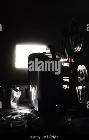 Old film projector and a glowing screen in the dark Stock Photo