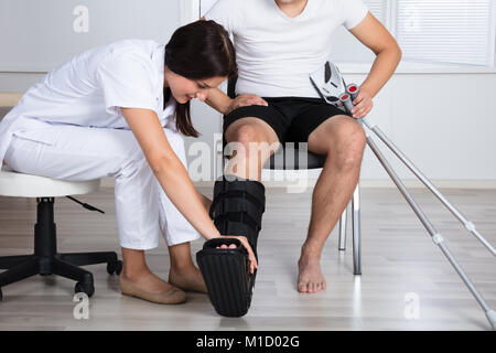 Young Female Doctor Putting Walking Brace On Person's Leg In Hospital Stock Photo