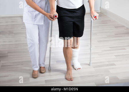 Female Physiotherapist Helping Injured Man To Walk With Crutches In Hospital Stock Photo