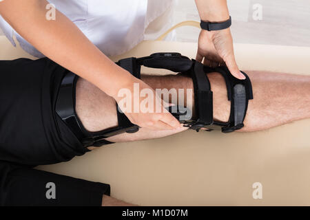 Female Physiotherapist Fixing Knee Braces On Man's Leg In Hospital Stock Photo