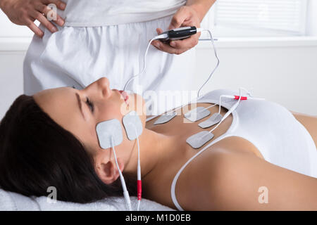 Close-up Of A Therapist's Hand Giving Electrodes Therapy On Young Woman's Chest And Face Stock Photo