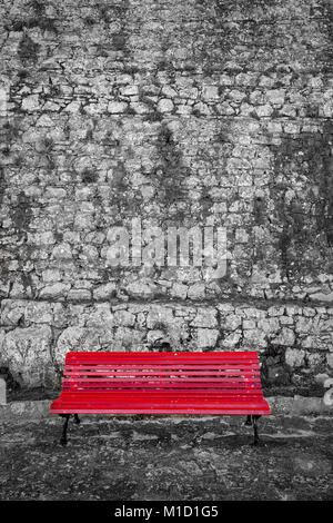 red painted bench against an old stone wall. Black and white and red. Stock Photo