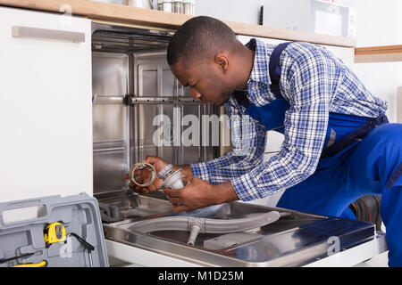 Young African Repairman Repairing Dishwasher In Kitchen Stock Photo