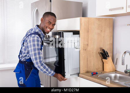 Male African Technician In Overall Installing Oven In Kitchen Stock Photo