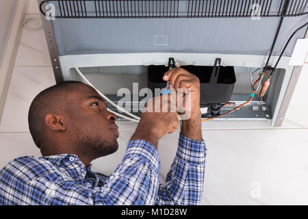 Young Male Serviceman Working On Fridge With Screwdriver At Home Stock Photo