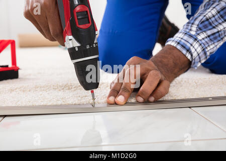 Person Hand Installing Carpet On Floor Using Wireless Screwdriver Stock Photo
