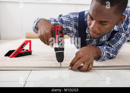 Person Hand Installing Carpet On Floor Using Wireless Screwdriver Stock Photo