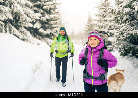 Happy teamwork couple hikers trekking in white winter woods and mountains. Young people walking on snowy trail with backpacks, healthy lifestyle adven Stock Photo
