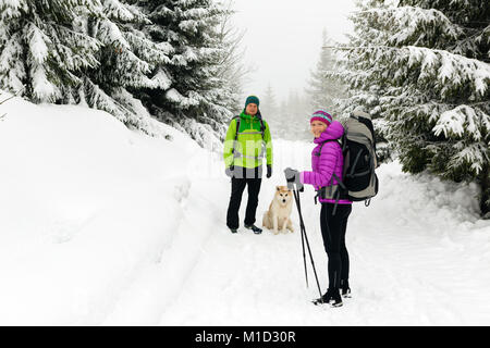 Man and woman happy teamwork couple hikers trekking in white winter woods and mountains. Young people walking on snowy trail with backpacks, healthy l Stock Photo