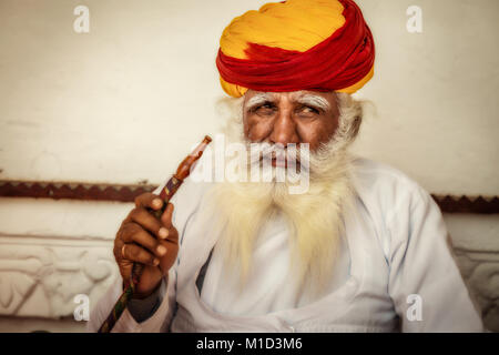 Aged man in traditional Rajasthani dress and colorful turban smoking a hookah at Mehrangarh Fort. Stock Photo