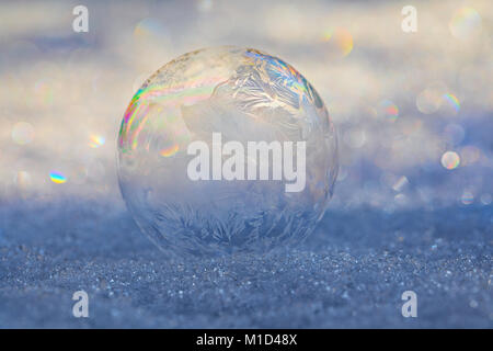 Frozen bubble on snow with ice crystals forming on the bubble and refracting light creating a prism pattern Stock Photo