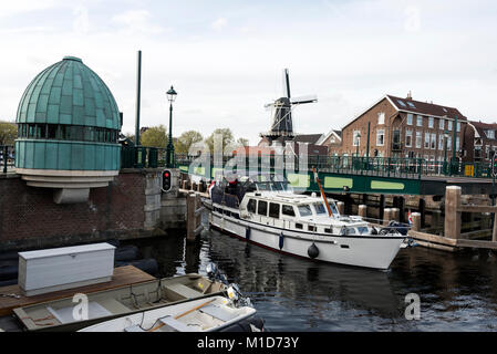 A drawbridge opens to allow a boat to pass on the Spaarne River in Haarlem, Holland.   In the distance is the Molen de Adriaan windmill Stock Photo