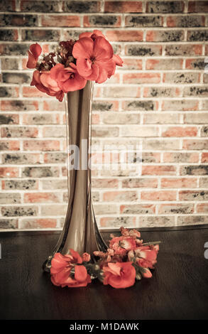 A tall vase with pink geraniums with a stone wall in the background Stock Photo