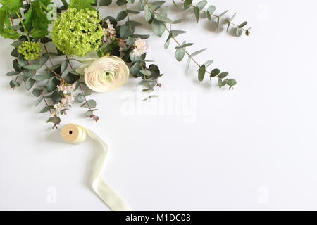 Feminine wedding, birthday desktop mock-up scene. Blank paper greeting card and bouquet of eucalyptus branches, pink roses and Persian buttercup flowers. White table background. Flat lay, top view. Stock Photo