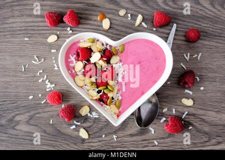 Healthy raspberry smoothie in a heart shaped bowl with superfoods. Above scene on a wood background. Stock Photo