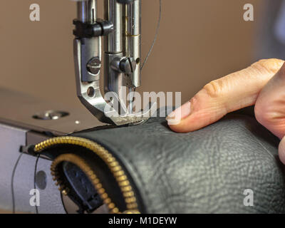 Industrial Sewing machine in action with hands working on leather garment Stock Photo