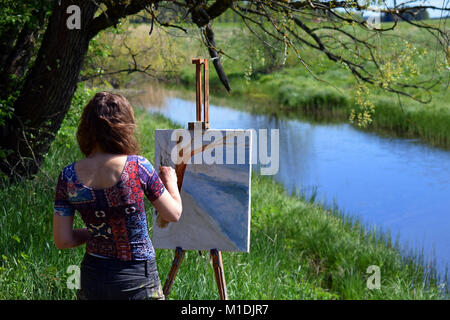 Female landscape artist paints a beautiful small river scene on canvas. Stock Photo