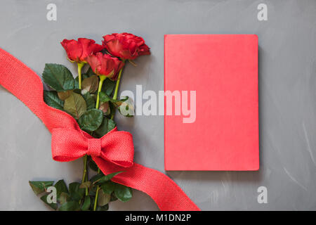 Valentine's card. Bouquet of red roses and red notebook on grey. Close up. Copy space. Top view. Stock Photo