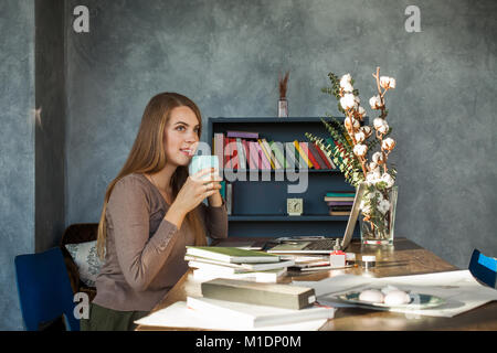Cute Woman Sitting in Office, Drinking Coffee and Using Laptop Stock Photo