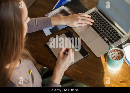 Young Designer Woman sitting at Home Office Desk and Using Graphic Tablet and Laptop Stock Photo