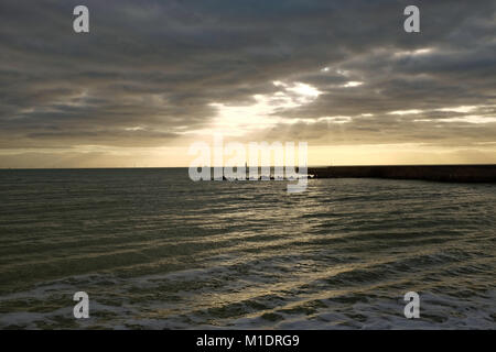 Sunlight breaking through dark clouds over the entrance to Port Shoreham, West Sussex, England, UK, as a small yacht approaches the harbour. Stock Photo