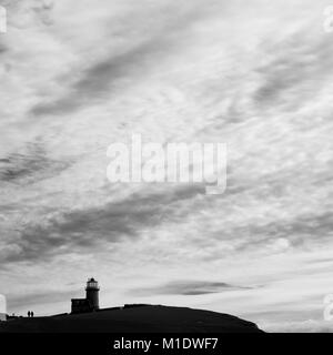 Couple walking beside Belle Tout lighthouse, Beachy Head, East Sussex, silhouetted against big sky with clouds Stock Photo