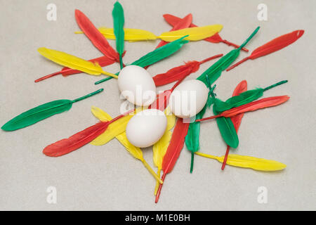 Natural white chicken eggs, green, red and yellow feathers on grey stone background. Easter still life, spring, summer, organic food, dieting Stock Photo