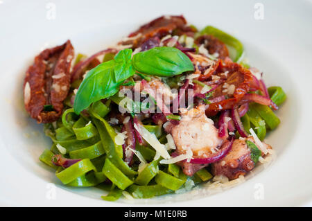green tagliatelle pasta with seafood, sun-dried tomatoes, red onion and parmesan Stock Photo