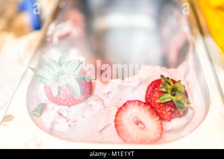 Macro closeup of pink red strawberry flavor gelato ice cream with whole fruit berry pieces on display in cafe store shop with scoop in Italy, Italian Stock Photo