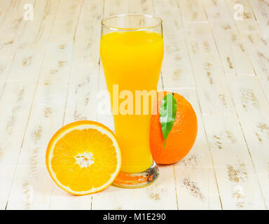 On the wooden surface stands a tall glass with freshly squeezed orange juice, lying next to a whole orange and half orange Stock Photo