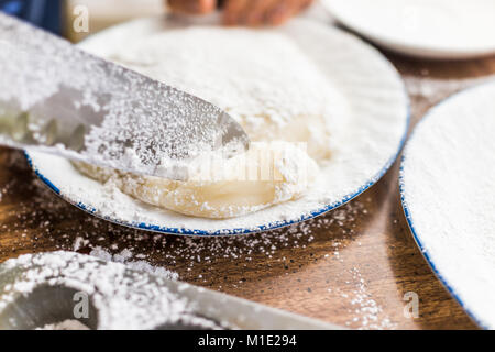 Kitchen knife cutting piece of mochi sticky glutinous rice cake dusted with starch flour to make dessert Stock Photo